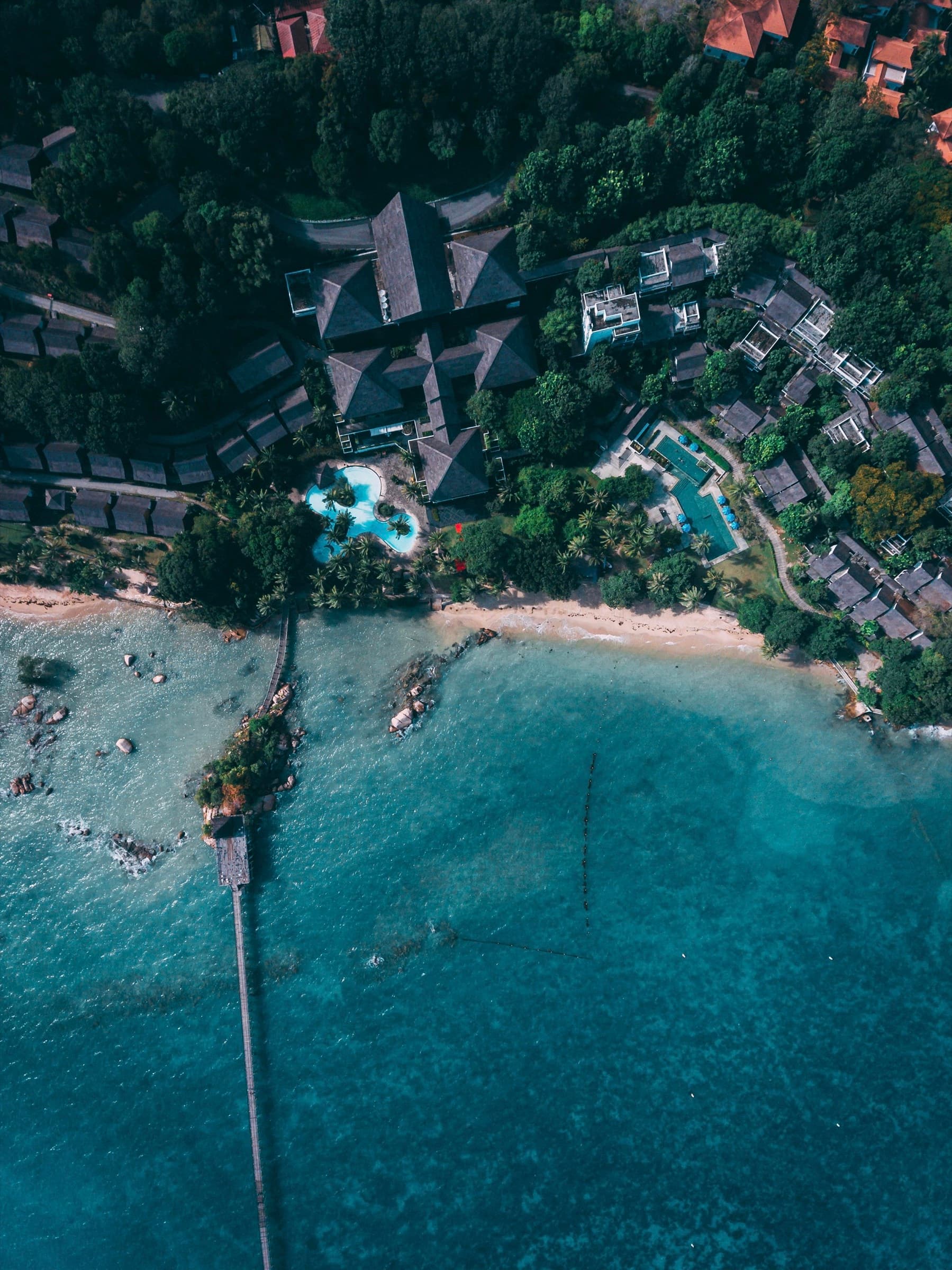 Aerial view of a coastal resort set into forest above a turquoise bay